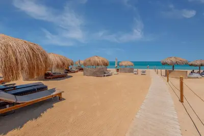 a beach with chairs and straw umbrellas and the ocean at Beach Front Paradise - 3 master beds - Abu Tig Marina - El Gouna in Hurghada