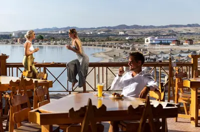 a man and two women sitting at a table on a deck at Three Corners Equinox Beach Resort in Abu Dabab