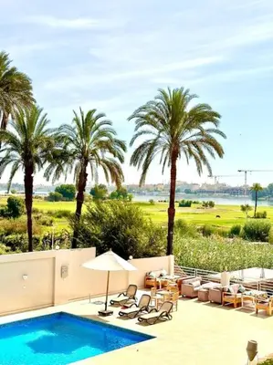 a swimming pool with chairs and palm trees in the background at Royal Nile Suites - Luxury Nile View 2 in Luxor