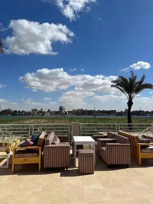 a patio with chairs and tables and a palm tree at Royal Nile Suites - Luxury Nile View 2 in Luxor
