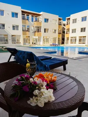 a table with a bowl of fruit and flowers on it next to a pool at Port Ghalib Apartments in Port Ghalib