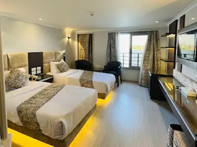 a hotel room with two beds and a desk at Nile Cruise from Aswan to Luxor 3 Night And Luxor to Aswan 4 Night in Jazīrat al ‘Awwāmīyah