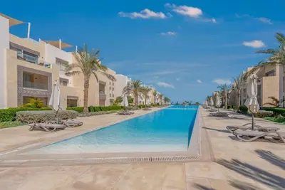 a pool at the resort with chaises and palm trees at Ground Floor 2BR Apt in Mangroovy, Pool & Beach in Hurghada
