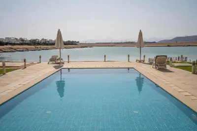 a swimming pool with umbrellas and a body of water at The Sandy Feet Sea Front in Hurghada