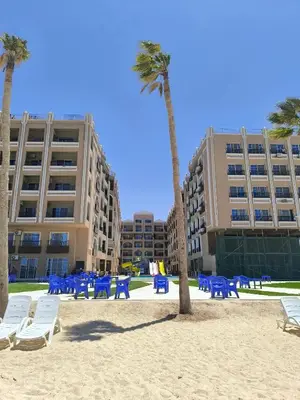 a beach with chairs and palm trees in front of a building at Terracotta studio with amazing beach and sea view in Hurghada