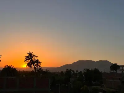 a sunset with palm trees and mountains in the background at Luxor Sun Villa in Luxor