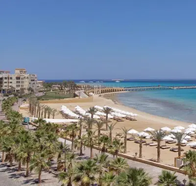 a beach with white umbrellas and palm trees and the ocean at Designer Loft mit grandiosem Meerblick am roten Meer in Hurghada