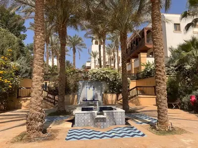 a fountain in front of a building with palm trees at Ancient Sands Golf Resort El Gouna Luxury Apartment in Hurghada