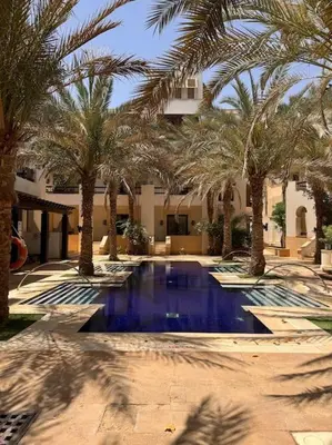 a swimming pool with palm trees in front of a building at Ancient Sands Golf Resort El Gouna Luxury Apartment in Hurghada