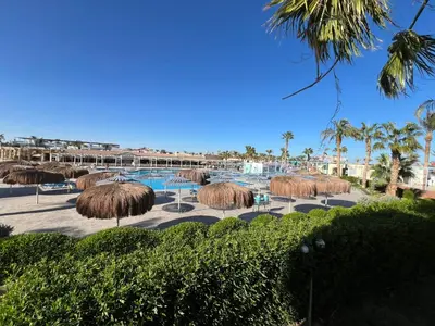 a resort with a pool and straw umbrellas and palm trees at Elegant 2-Bedroom Suite Mirage Bay in Hurghada