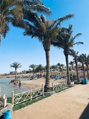 a beach with palm trees and people walking in the water at Apartment in el karma aqua beach resort hurghada near el gouna 2 in Hurghada