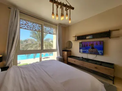 a bedroom with a bed and a tv and a window at Mangroovy Serinity 2br pool view in Hurghada