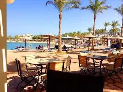 a group of tables and chairs on a beach with palm trees at شاليه في منتجع ميراج in Hurghada
