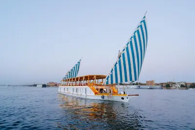 a boat with blue and white sails on the water at Turquoise Dahabiya , 3,4,7 nights sailing between Luxor and Aswan in Luxor