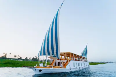 a white boat with blue sails on the water at Turquoise Dahabiya , 3,4,7 nights sailing between Luxor and Aswan in Luxor