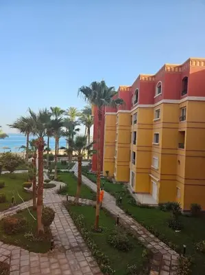 a yellow building with palm trees in front of it at Esplanada flat with free beach, no single men in Hurghada