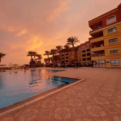 a swimming pool in front of a building with palm trees at Esplanada flat with free beach, no single men in Hurghada