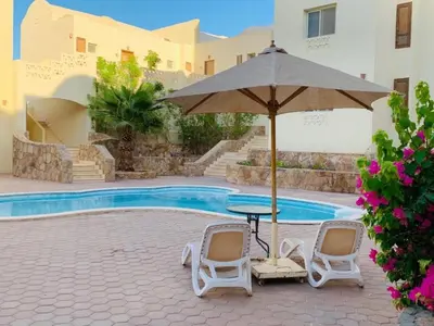 a table with two chairs and an umbrella next to a pool at Makadi Heights lovely flat in Hurghada