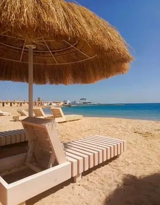 a beach with a straw umbrella and chairs and the ocean at Princess Resort Hurghada in Hurghada