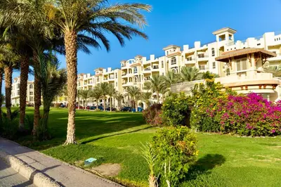 a large white building with palm trees and flowers at El Andalous Sea View Apartment Sahl Hasheesh in Hurghada