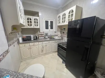 a kitchen with a black refrigerator and white cabinets at Happy home in Hurghada