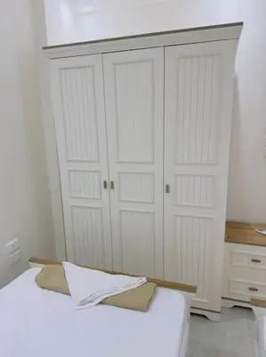 a white bedroom with a bed and two white cabinets at Moly House in Aswan