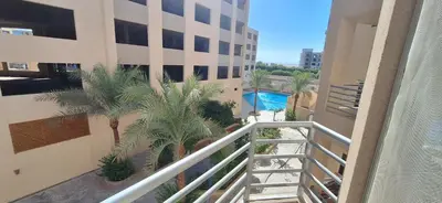 a balcony of a building with palm trees and a swimming pool at Cozy 1BR in Princess Resort with Pools & Private Beach in Hurghada