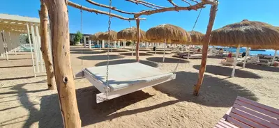 a swing on a beach with straw umbrellas at Cozy 1BR in Princess Resort with Pools & Private Beach in Hurghada