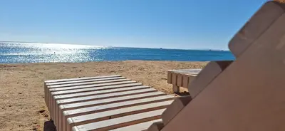two benches sitting on the beach near the water at Cozy 1BR in Princess Resort with Pools & Private Beach in Hurghada