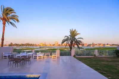 a patio with tables and chairs and palm trees at Royal Nile Suites - Nile View 2 in Al Aqālitah