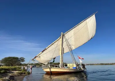 a boat with a large sail in the water at The Adventures of Aga Khan in Aswan