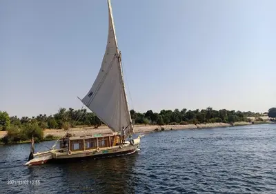 a boat with a large sail in the water at The Adventures of Aga Khan in Aswan