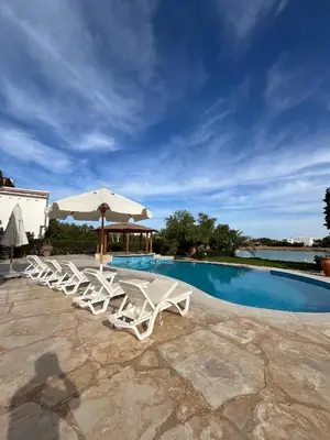 a group of lounge chairs and an umbrella next to a swimming pool at white villa 4 bedroom elgouna heated pool in Hurghada
