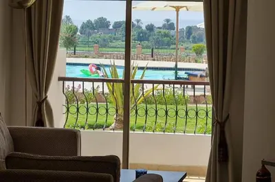 a living room with a view of a pool through a window at Nile Front Luxor Apt Sleeps 6 with Pool in Luxor