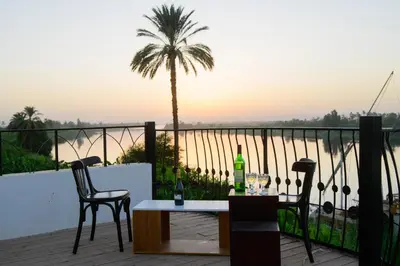 a table and chairs on a balcony with a palm tree at Eyaru Palace Nile View in Luxor