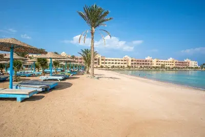 a beach with benches and a palm tree and a building at Tiba gollden resort in Hurghada