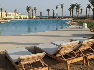 two lounge chairs and a swimming pool with palm trees at 2BR Somabay Twin Villa in Mesca Near Beach & Pools in Hurghada