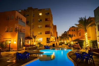 a swimming pool with blue chairs and buildings at night at Al Dora Residence Apartments in Hurghada