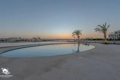 an empty swimming pool with palm trees and the sunset at Tranquil 2BR in Shedwan I El Gouna I Pool and Lagoon View in Hurghada