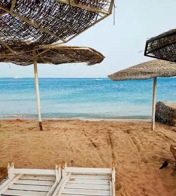 a beach with two straw umbrellas and the ocean at Lux Gardenhouse pool WiFi Private garden Hurghada in Hurghada