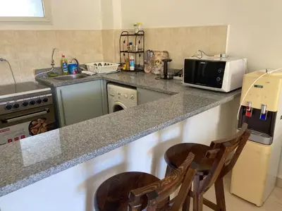 a kitchen with a counter with a microwave and two chairs at Lovely flat with balcony and shared pool in Hurghada