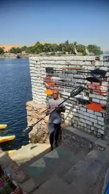 a man holding a paddle in front of a stone wall at Dangy Kato in Aswan