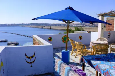 a patio with a blue umbrella and chairs and water at dahab in Aswan