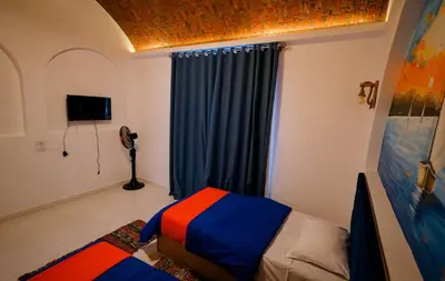 a bedroom with a bed with blue curtains and a television at JAREEDY Guest house in Shellal