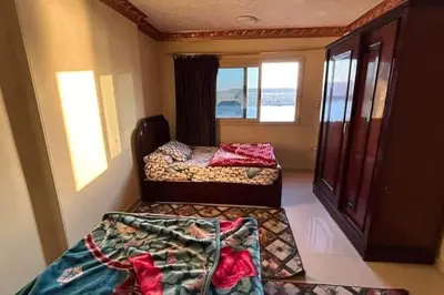 two beds in a small room with two windows at The best view of the Nile in Naj‘ al ‘Amrāb