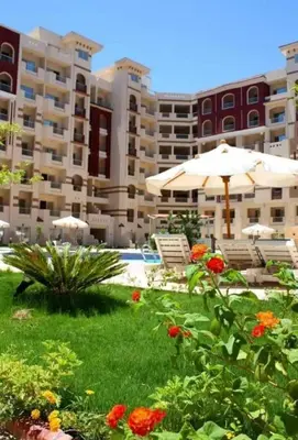 a lawn with chairs and an umbrella and some flowers at Florenza khamsin Apartment in Hurghada