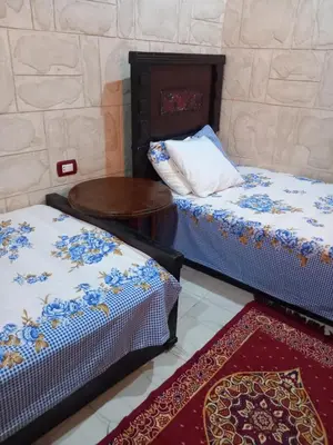 a room with two beds and a table and a rug at Hashem Nubian Guest House in Aswan