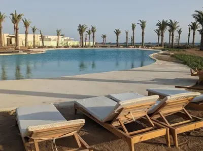 two lounge chairs and a swimming pool with palm trees at Somabay Seaview 1BR Loft 2 Mins to Beach & Pool in Hurghada