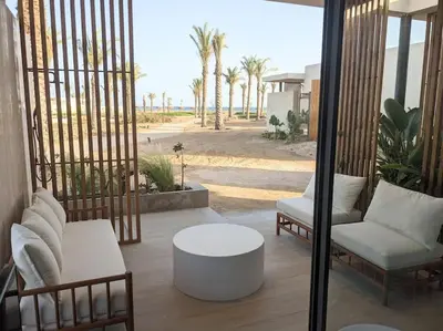 a patio with two chairs and a coffee table and palm trees at Magical Cabana Steps From Beach & Pool in Hurghada