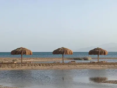 three straw umbrellas and benches on a beach at Somabay 2BR Grand Cabana Minutes From Pool & Sea in Hurghada